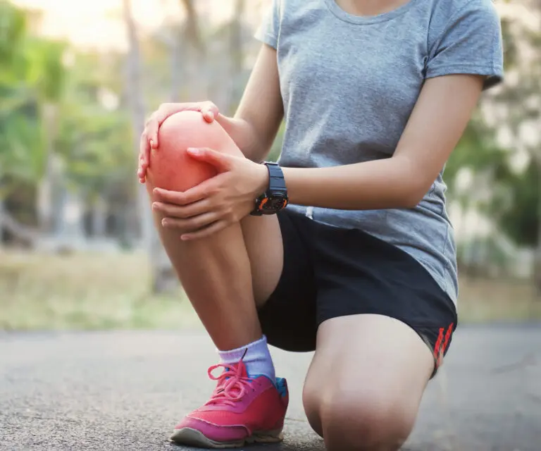 Sportlerin kniet am Boden und hält sich das schmerzende Knie