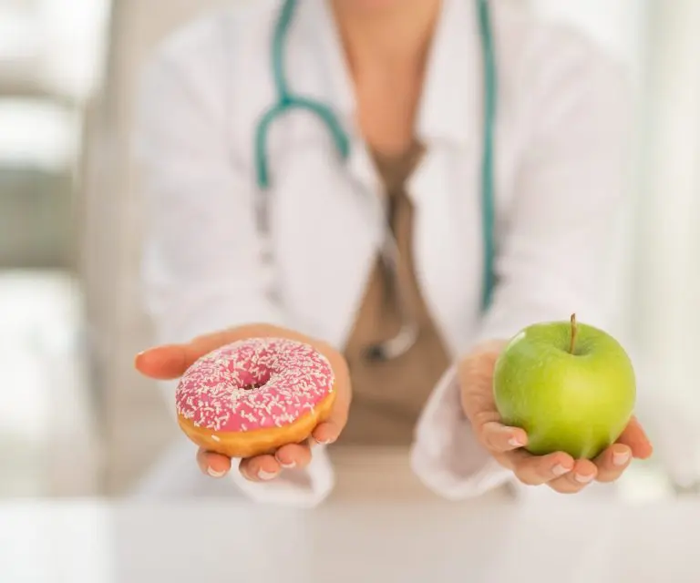 Ärztin hält einen Donut in der einen und einen Apfel in der anderen Hand