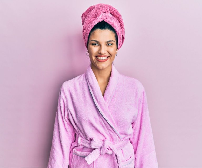 Junge Frau trägt Duschtuch und Bademantel mit einem glücklichen Lächeln auf dem Gesicht.